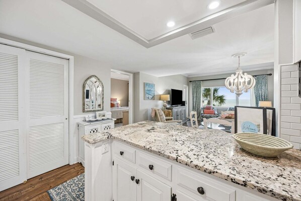 A kitchen with white cabinetry, a granite countertop, and a view of the ocean through the window.