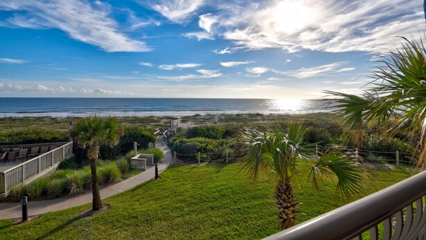 Een kustgezicht vanaf een balkon met uitzicht op een strand, met een pad naar een zithoek.
