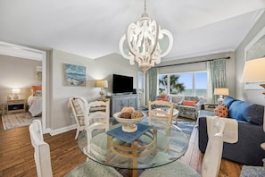 A spacious living room with a glass-top coffee table, a chandelier, and a view of the ocean through large windows. - Sandcastle Retreat - Hosted by Moore AI Rentals (Fernandina Beach)
