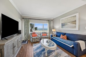 Una sala de estar con televisor, sofá, sillón, mesa de centro y vista al mar.