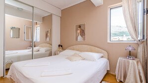 A bedroom with a large bed, a bedside table with a lamp, a mirror, and a window with curtains.