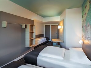 Ett hotellrum med en säng, ett skrivbord, en stol, en garderob och en hylla som är monterad på väggen.