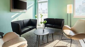 Un área de espera moderna con pared color turquesa, sofás de cuero negro, una mesa redonda y un sillón blanco.