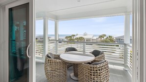 A covered outdoor area with a round table and wicker chairs, overlooking a beach and ocean view. - The Pelican`s Nest Egg - Hosted By Moore AI Rentals (Fernandina Beach)