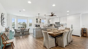 A spacious kitchen with a central island, white cabinetry, and a dining area with a wooden table and chairs. - The Pelican`s Nest Egg - Hosted By Moore AI Rentals (Fernandina Beach)