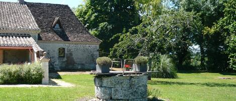 A rustic stone building with a tiled roof, surrounded by lush greenery and a well-maintained lawn.