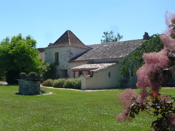 A traditional stone building with a tiled roof, surrounded by a well-maintained lawn and flowering plants.