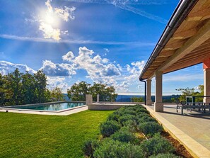 A modern outdoor pool area with a clear sky and a view of the sea.