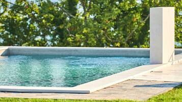 A rectangular swimming pool with a clear blue water surface, surrounded by a paved deck and a grassy area.