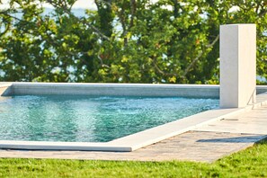 Una piscina rectangular con superficie de agua azul cristalina, rodeada por un deck pavimentado y una zona de césped.