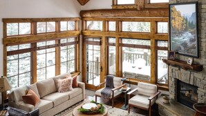 A cozy living room with a stone fireplace, large windows, and wooden beams. - Hot Tub| Ski-In/ Ski-Out | Sonos Sound (Big Sky)