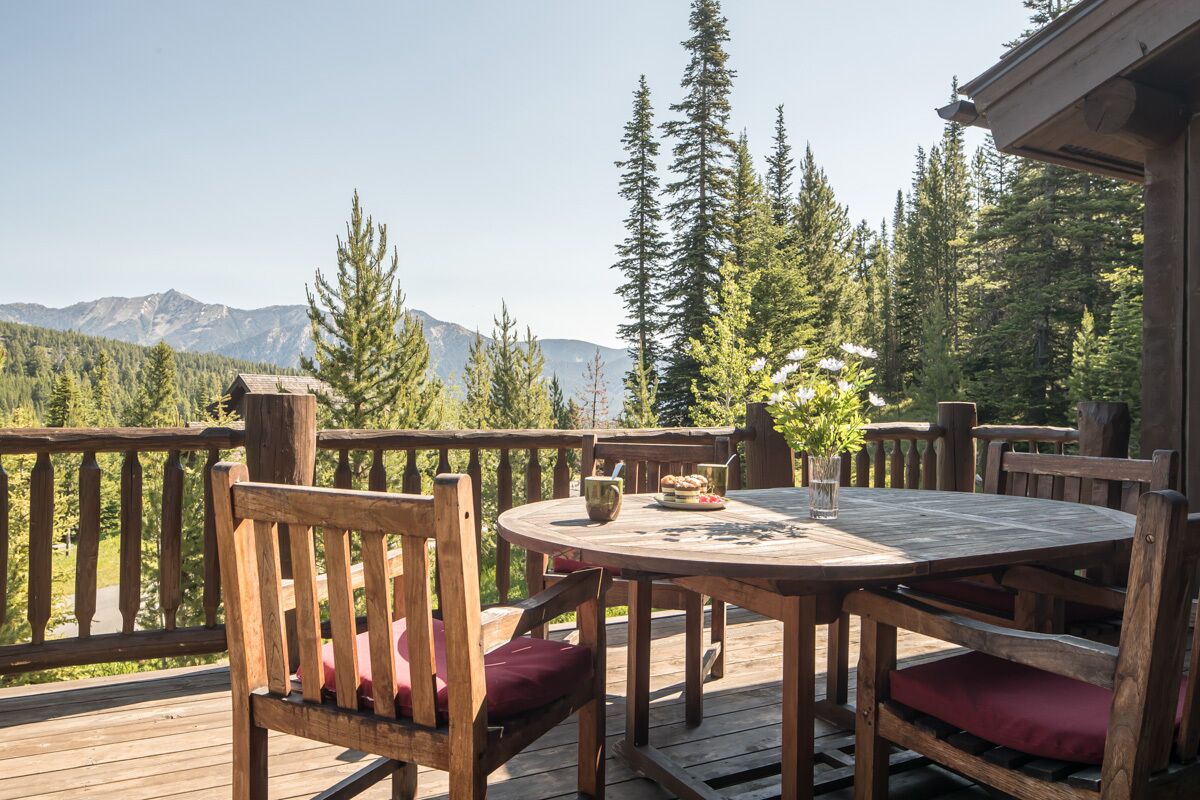 Una terraza de madera con una mesa redonda y sillas, con vistas a un bosque y montañas.