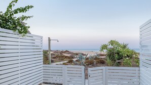 Um alpendre à beira-mar com grades brancas, um tapete amarelo, um balde de metal e vista para a praia e oceano.