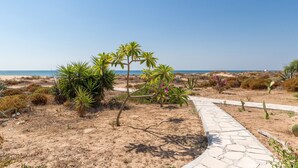 Uma trilha pavimentada que conduz a uma praia com vegetação rasteira e céu claro.