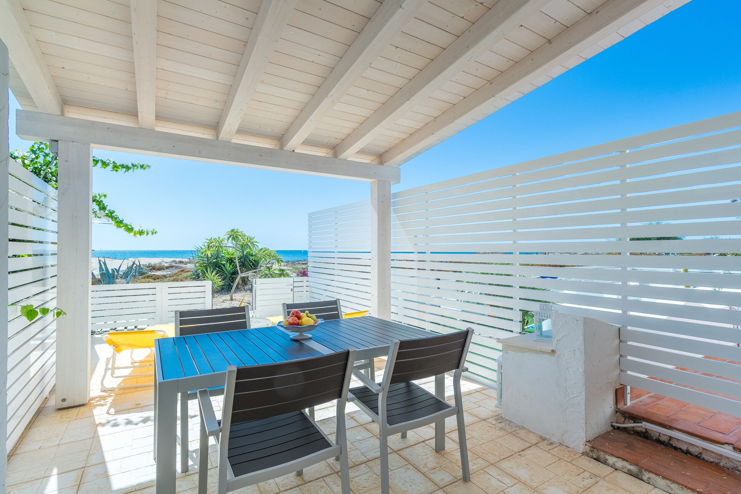 Un espacio de estar cubierto al aire libre con una mesa y sillas, con vistas a la playa.