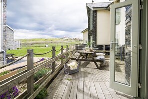 Une terrasse en bois avec des tables de pique-nique et un muret en pierre.