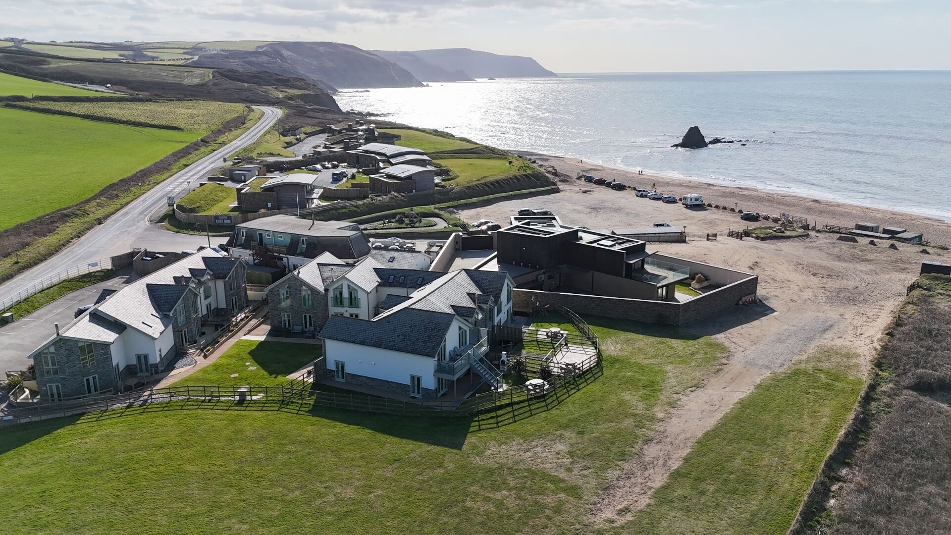 A coastal property with multiple buildings, a parking area, and a beach.