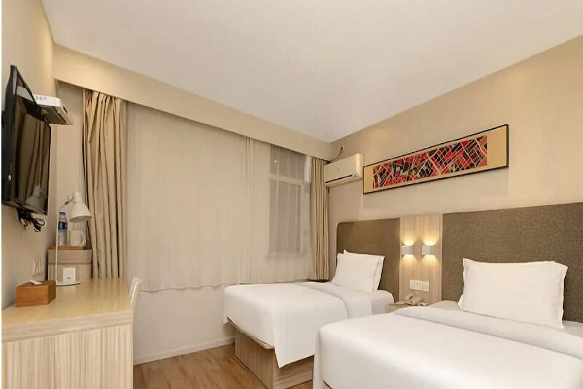 Ein Hotelzimmer mit zwei Betten, einem Schreibtisch, einer Lampe, einer Klimaanlage und einem Wandbild.