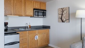 A compact kitchen with wooden cabinets, a stainless steel microwave, a coffee maker, and a refrigerator. - DT~ Free parking~ Sunset river views~ WiFi~ W/D (Wilmington)