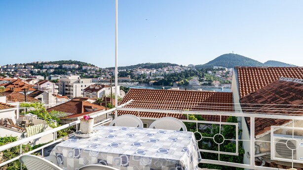 A terrace with a table and chairs, overlooking a cityscape with terracotta rooftops and a hill in the distance. - Apartment & Rooms Alan (Dubrovnik)