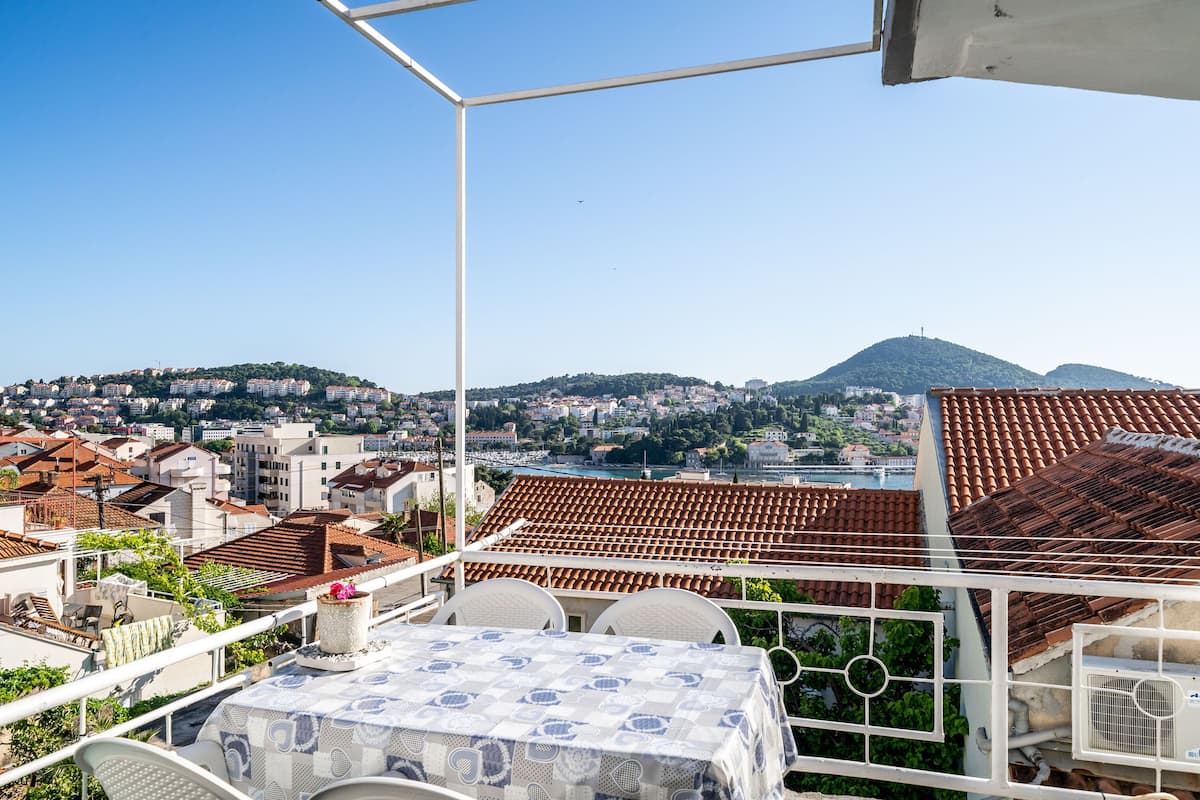 A terrace with a table and chairs, overlooking a cityscape with terracotta rooftops and a hill in the distance.
