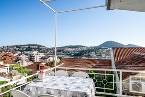 A terrace with a table and chairs, overlooking a cityscape with terracotta rooftops and a hill in the distance. - Apartment & Rooms Alan (Dubrovnik)