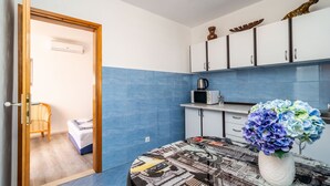 A compact room with a bed, a small kitchenette, and a dining area with a table and vase. - Apartment & Rooms Alan (Dubrovnik)