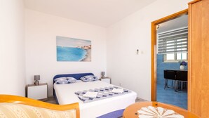 A bedroom with a bed, bedside tables, a painting, a dining area with chairs, and a wooden door. - Apartment & Rooms Alan (Dubrovnik)