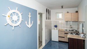 A compact kitchen with a blue accent wall, white cabinetry, and a small window. - Apartment & Rooms Alan (Dubrovnik)