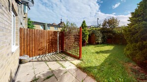 A residential backyard with a wooden fence, a paved pathway, and a grassy area. - Amazing 2 Bed House w/ Private Parking & Private Garden (London)