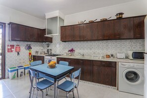 Cucina con mobili in legno, lavatrice, forno a microonde e zona pranzo con sedie e tavolo.