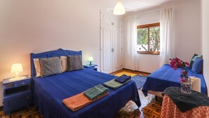 Une chambre avec deux lits, une table de chevet avec une lampe, une fenêtre avec des rideaux et une vue sur les arbres à l’extérieur.