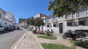Une rue pavée bordée de voitures garées, d’une moto et d’un banc.
