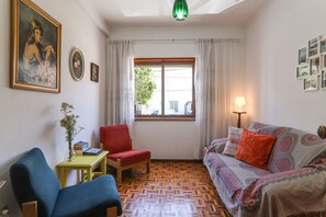 Una stanza con pavimento in parquet di legno, una sedia rossa, un divano blu, un tavolino con un vaso e una finestra con tende.