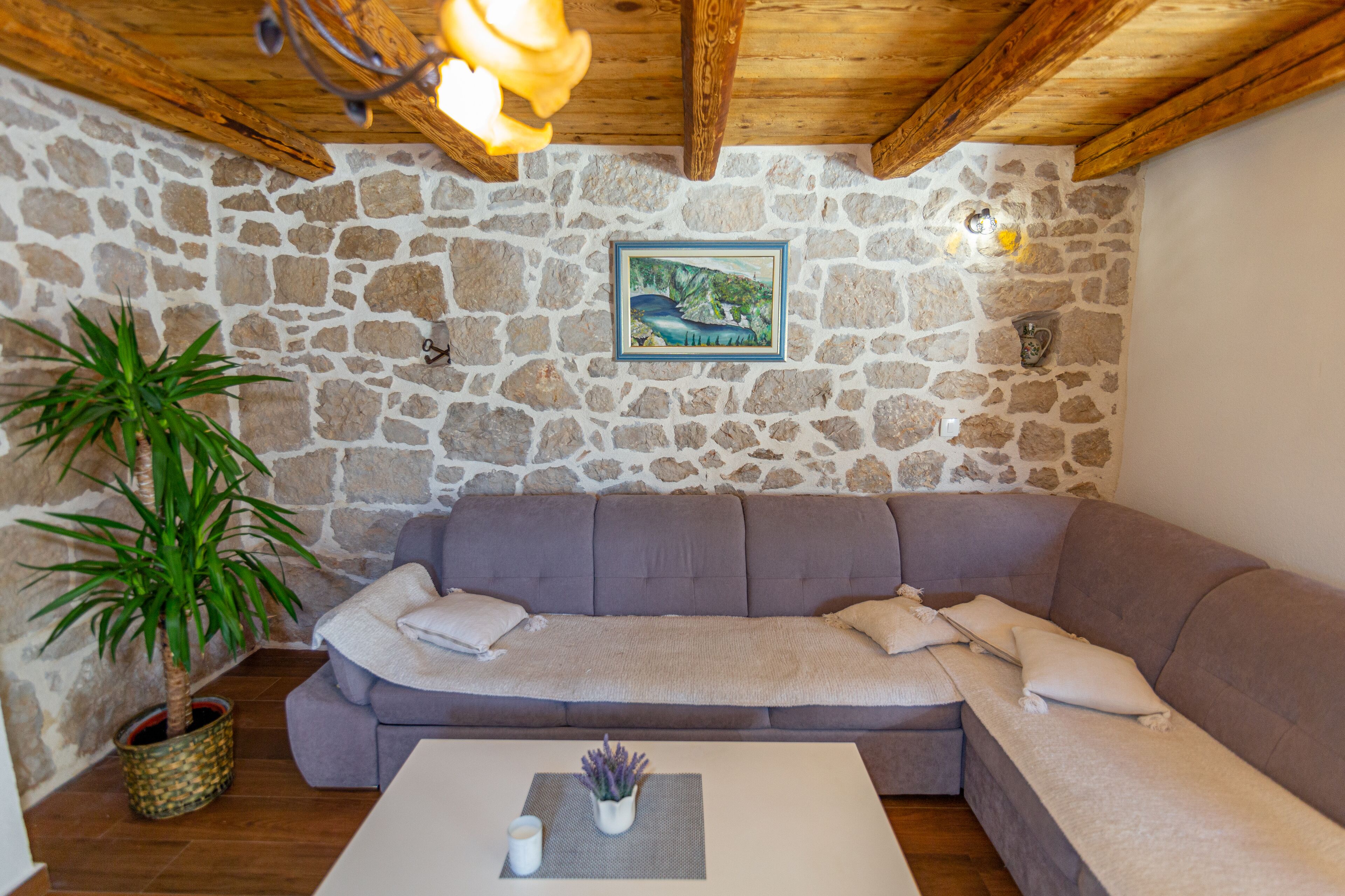 A cozy room with a stone wall, a gray sofa, a wooden ceiling, and a potted plant.