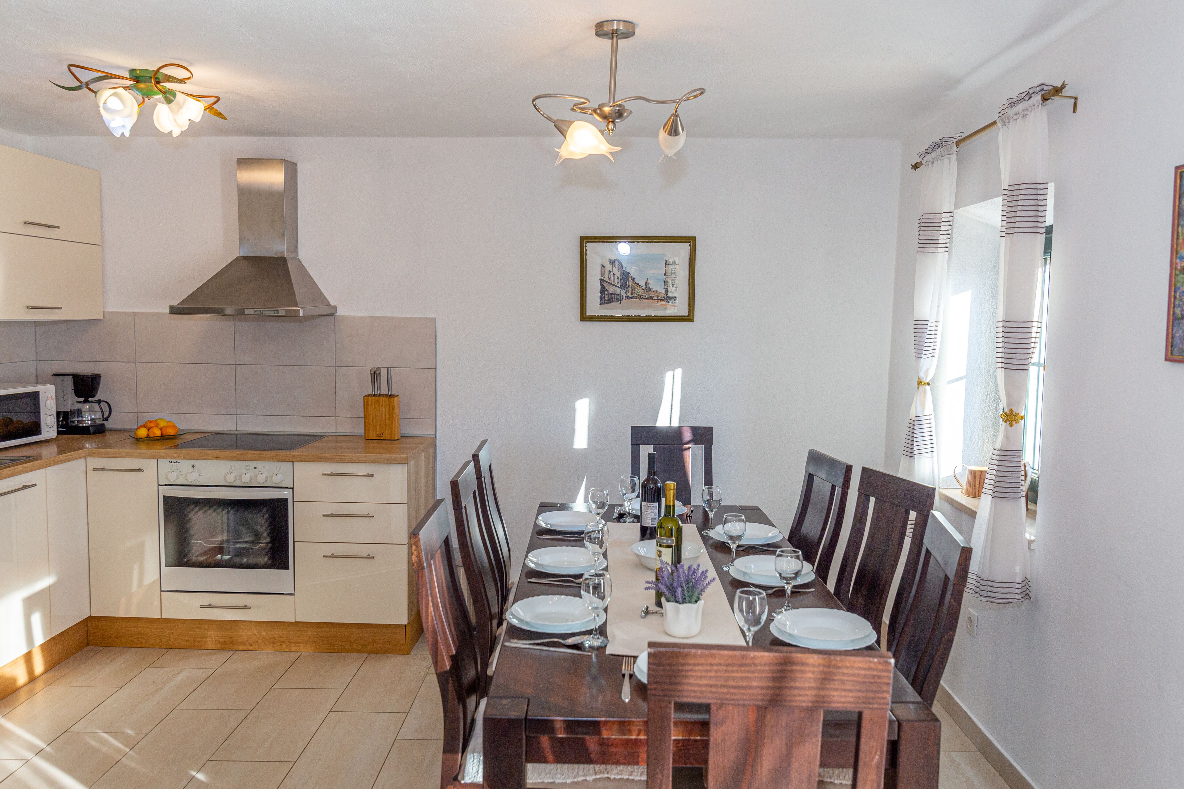 Una cocina moderna con armarios blancos, horno empotrado y comedor con una mesa de madera dispuesta para seis comensales.