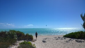 Une plage de sable fin, avec une eau d’un bleu limpide, et une personne qui marche en direction de la mer.