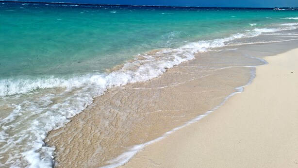 Una playa con agua turquesa cristalina, olas suaves y una orilla arenosa.