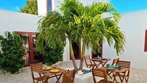 Un patio con una mesa y sillas de madera, rodeado por una palmera pequeña y otra vegetación.