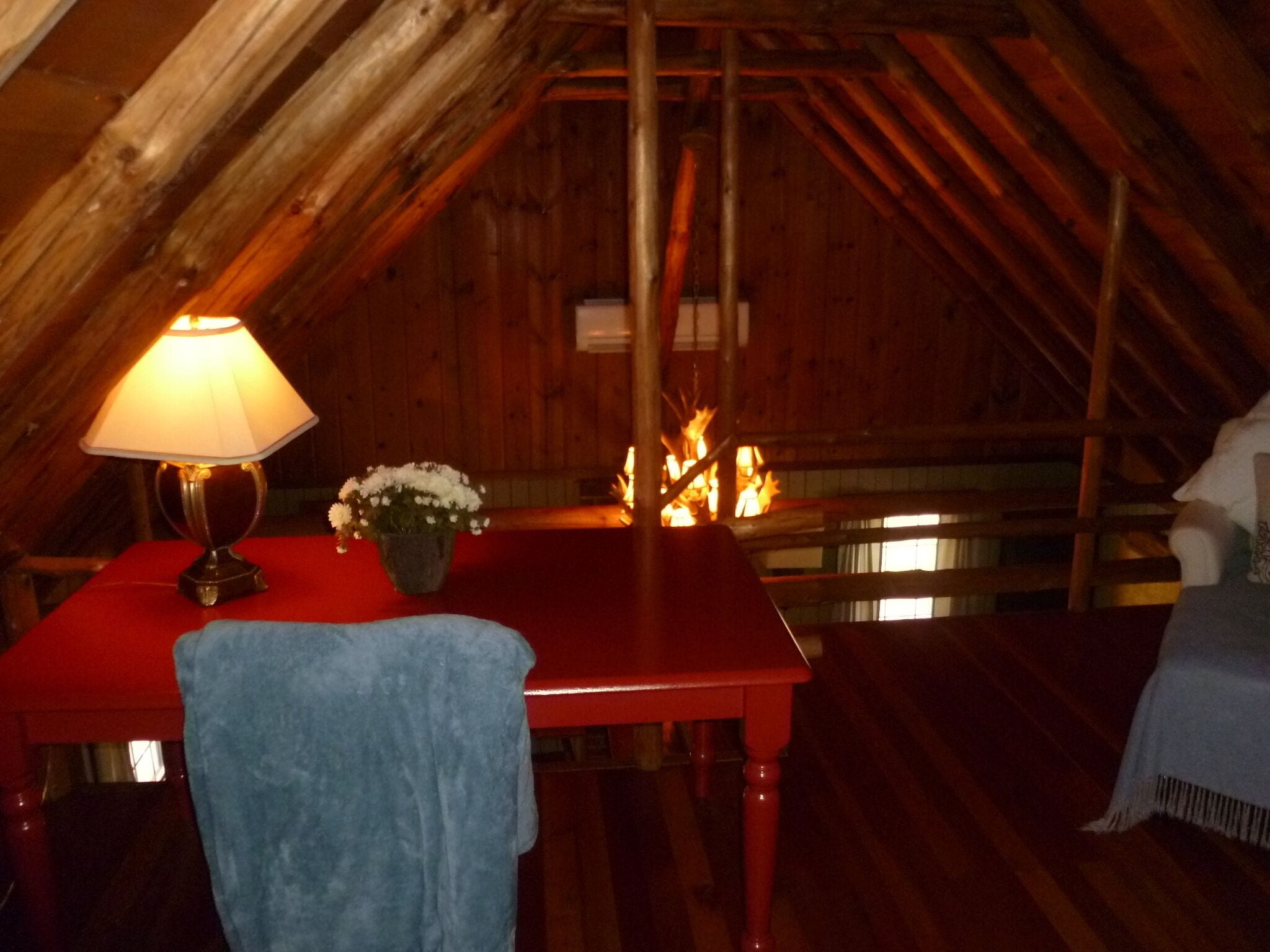 Una camera mansardata accogliente, con soffitto in legno, un tavolo con una lampada, un vaso di fiori e un fuoco che arde sullo sfondo.