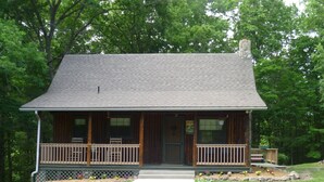 A two-story log cabin with a front porch, a chimney, and a small garden area with flowers.