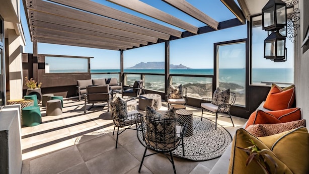 A modern outdoor seating area with a view of the ocean and mountains. - Belle Maroc (Cape Town)