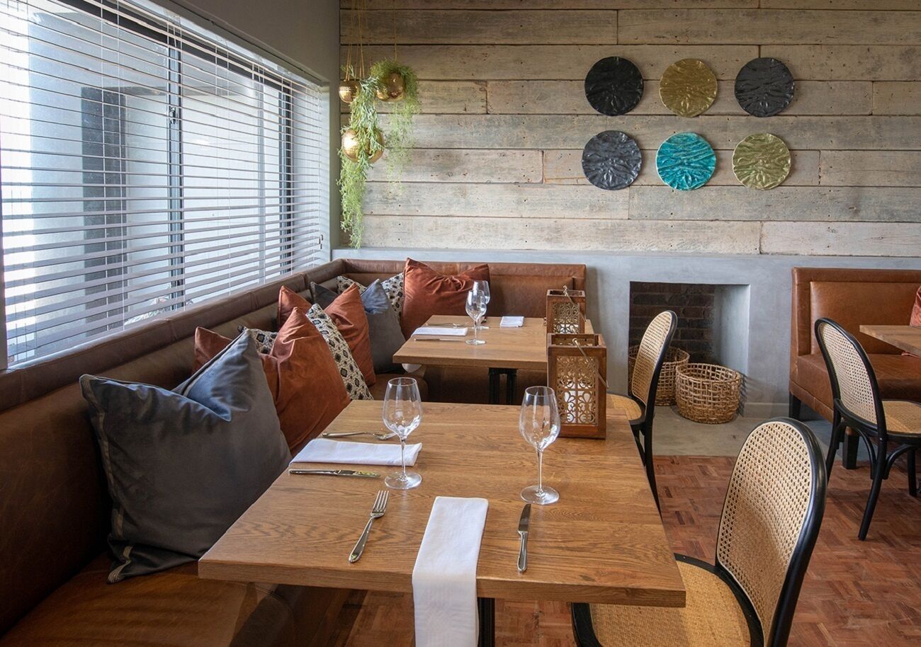 A cozy restaurant with wooden tables, cushioned seating, and a rustic brick wall.
