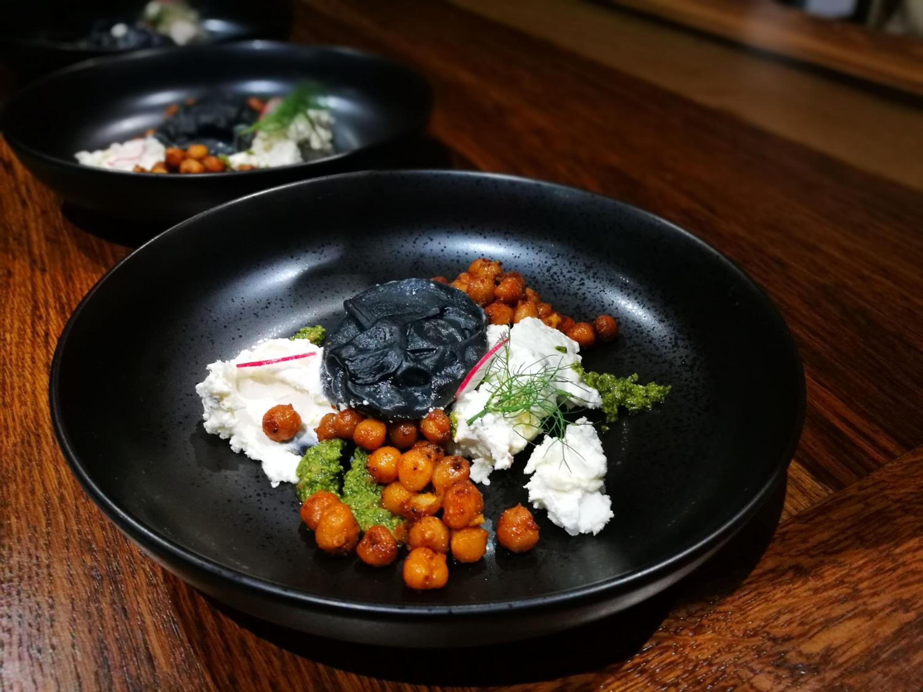 Dos platos negros con comida sobre una mesa de madera.
