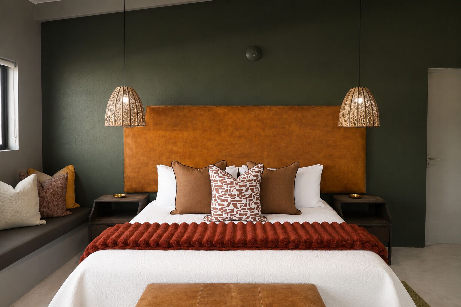 A bedroom with a large bed, two bedside tables, a headboard, and two hanging lamps.