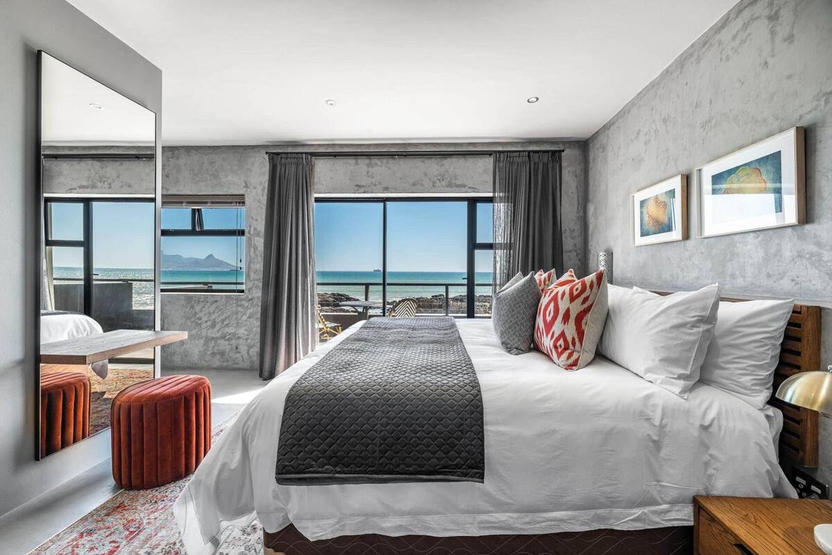 A modern bedroom with a large bed, a view of the sea, and a balcony.