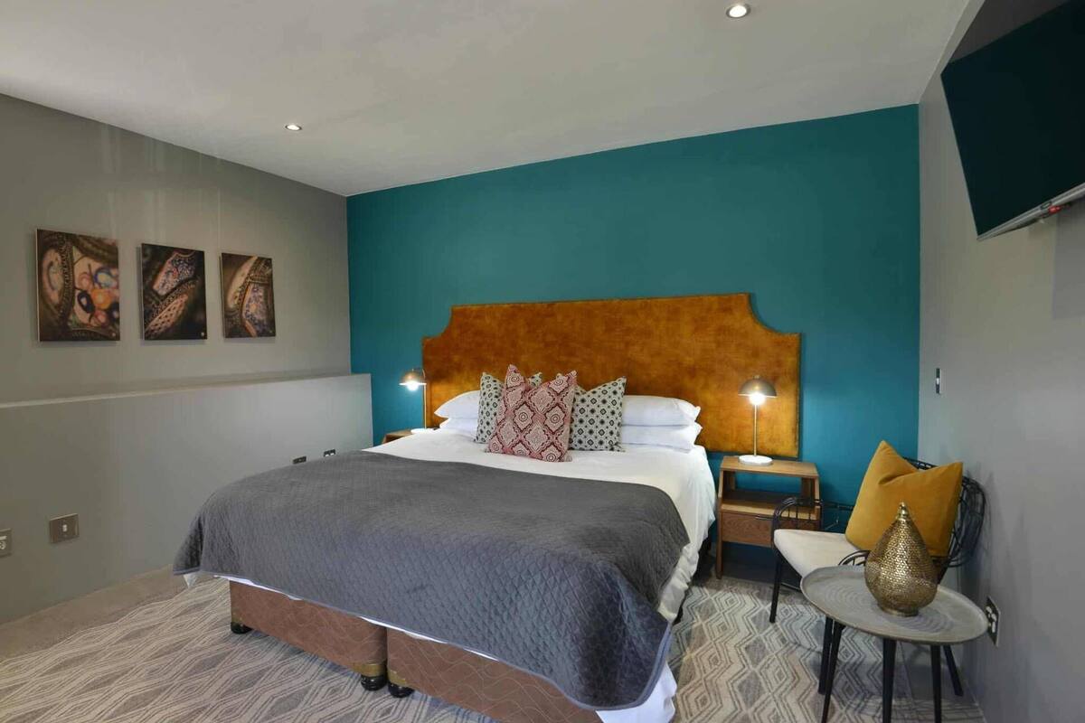 A modern hotel room with a large bed, teal accent walls, and a wooden headboard.