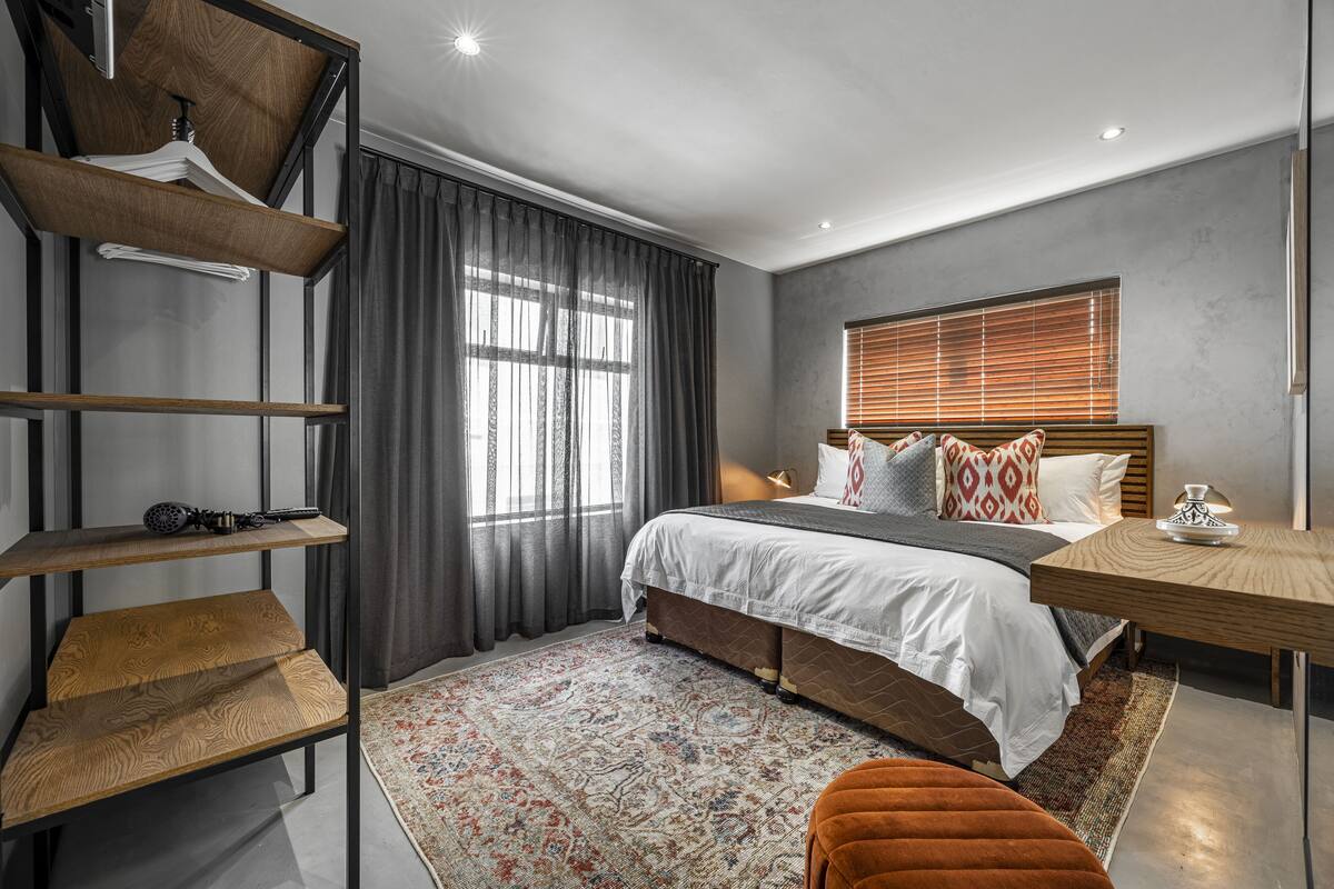A modern bedroom with a bed, a wooden side table, a hanging rack, and a patterned rug.