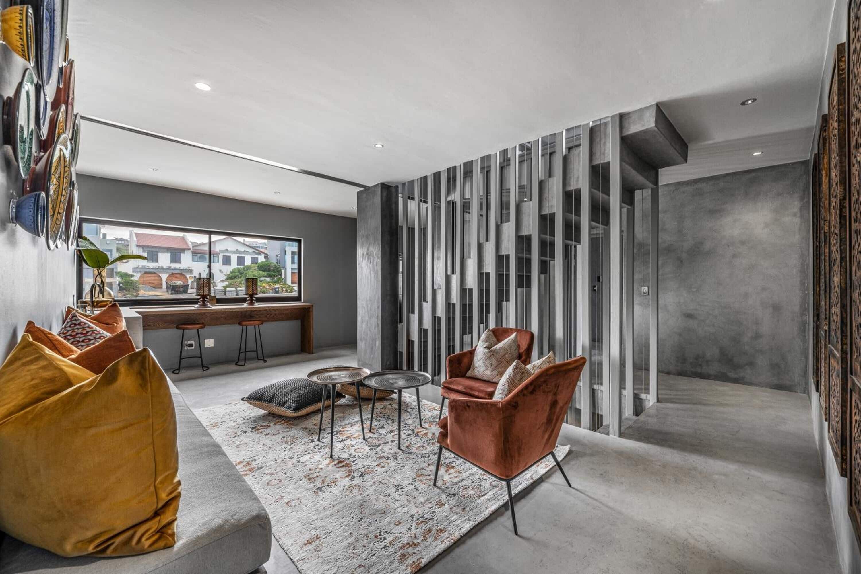 A modern living room with a sofa, coffee table, and a chair. There is a large window with a view of buildings outside.