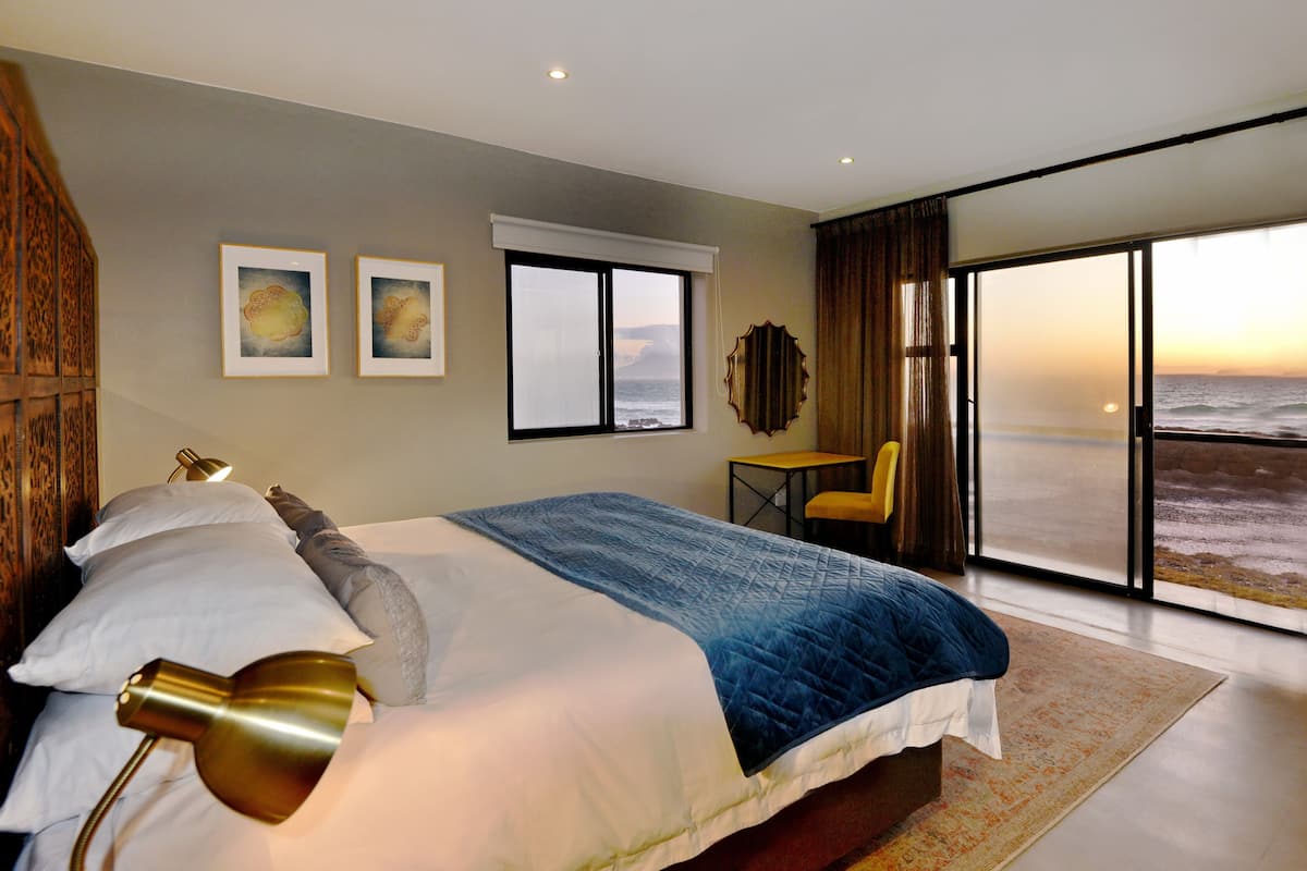 A modern hotel room with a large bed, a desk, and a view of the ocean.